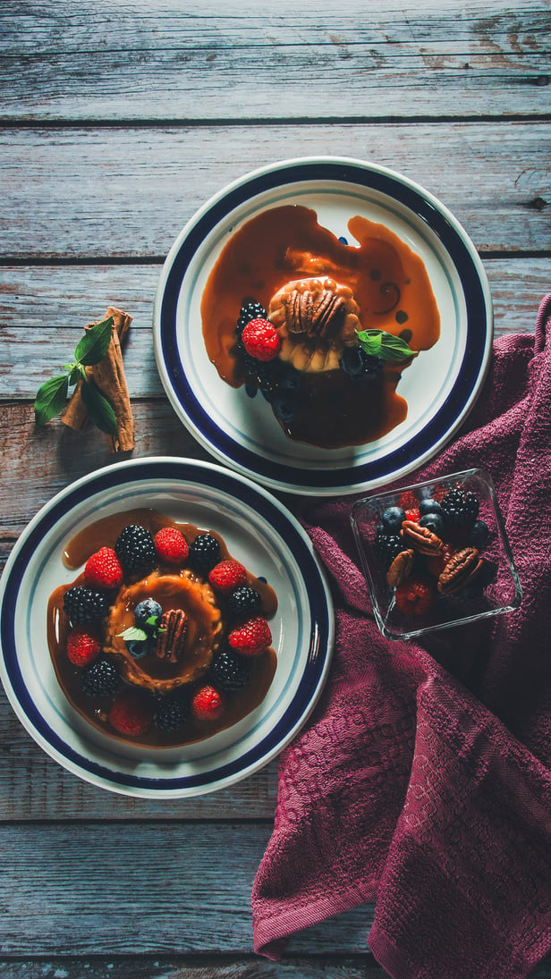 Plates of Flan with Berries, Pecans and Caramel Sauce